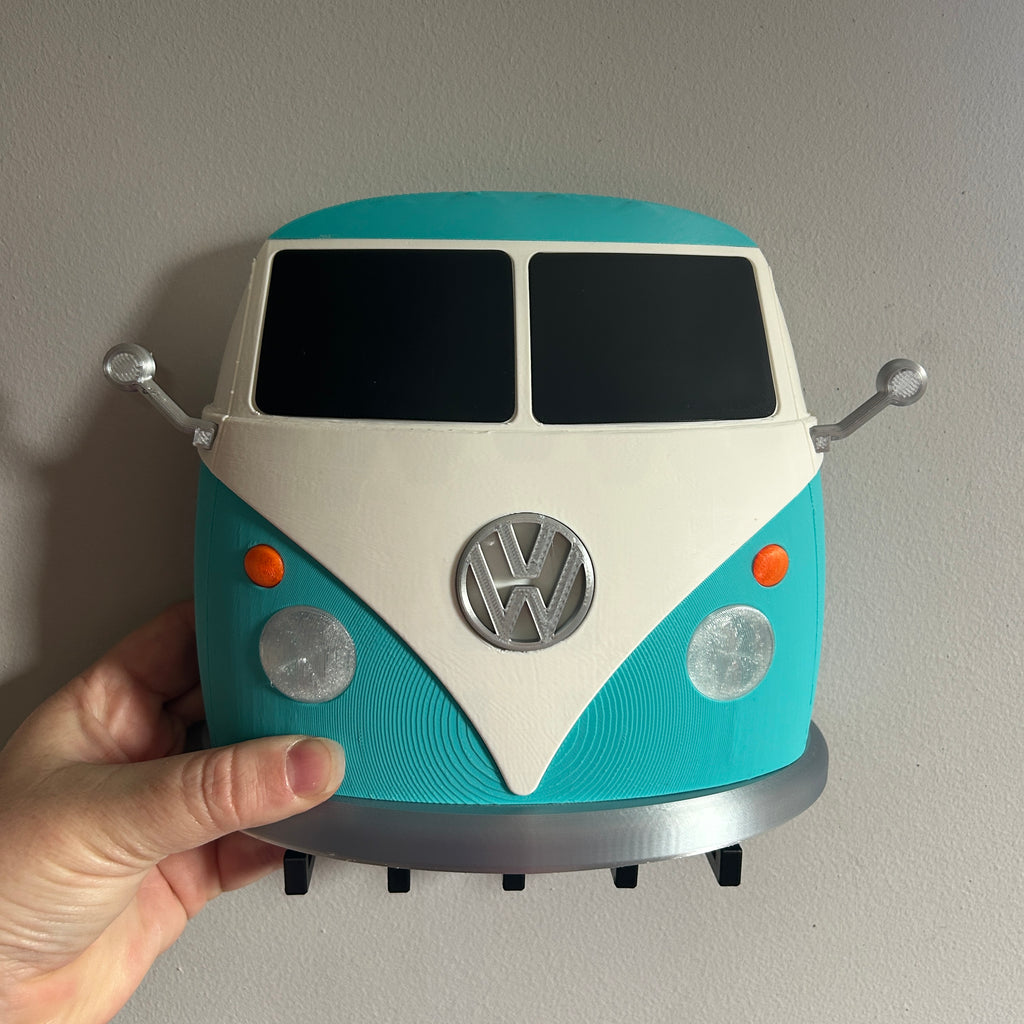 A hand holding a 3D-printed wall clock shaped like a retro Type 2 van, featuring a turquoise and cream color scheme with silver details.