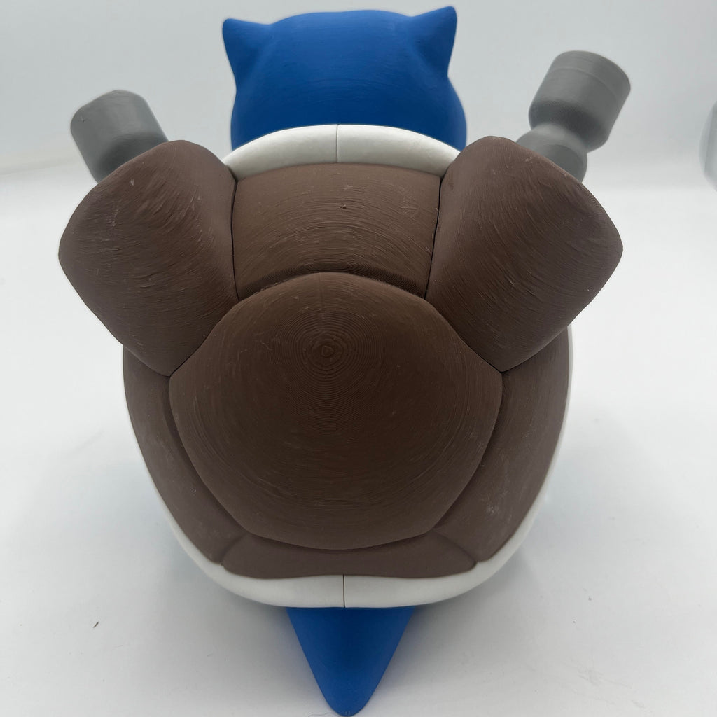 A toy figure shown from the back, featuring a brown shell, blue head and tail, and gray limbs, photographed on a plain white studio background.