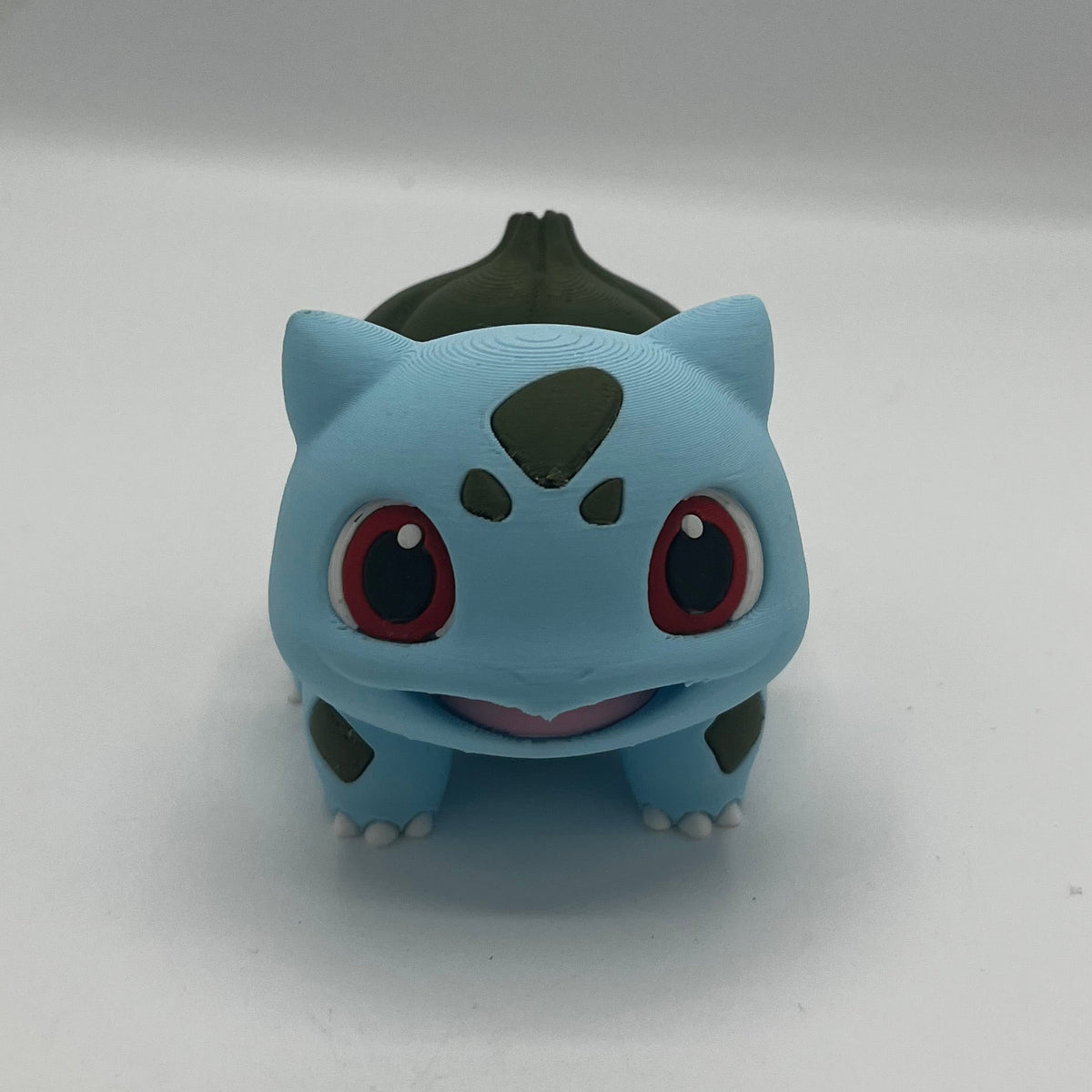 A small blue and green Bulbasaur figurine standing upright on a plain light background.