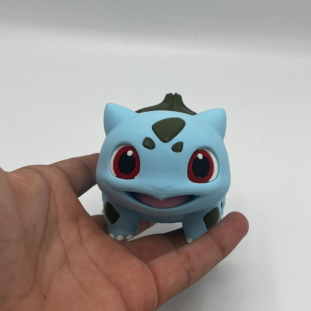 A small blue and green Bulbasaur figurine resting on an open hand to show its size, against a plain white background.
