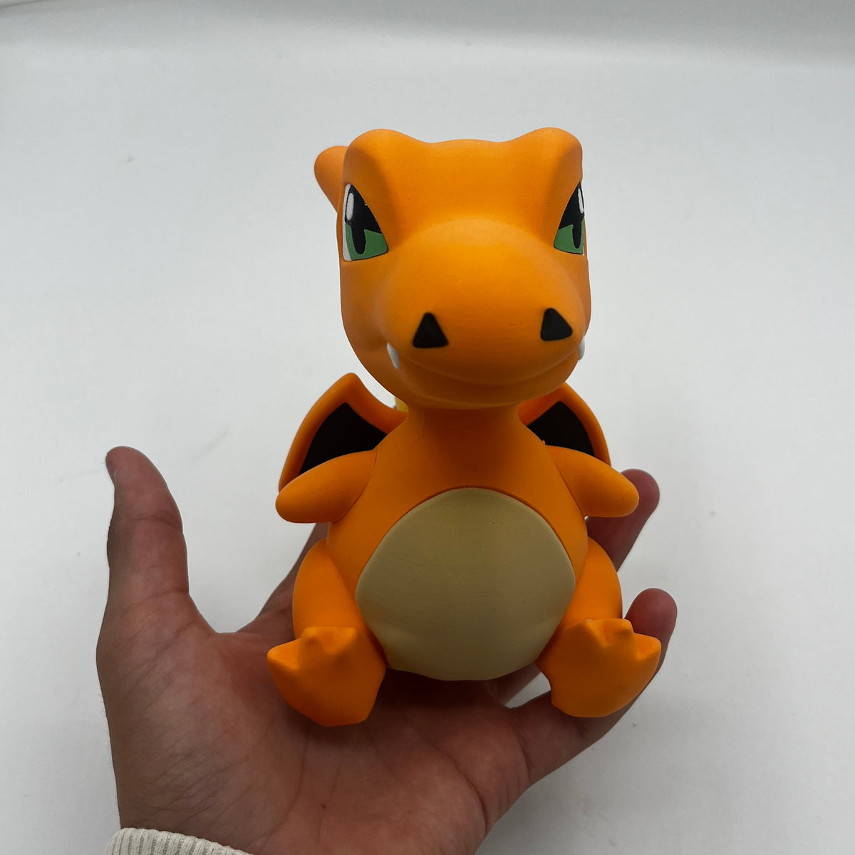 An orange Charizard toy figure with a beige belly and black wings, held in a person's hand against a plain white background.