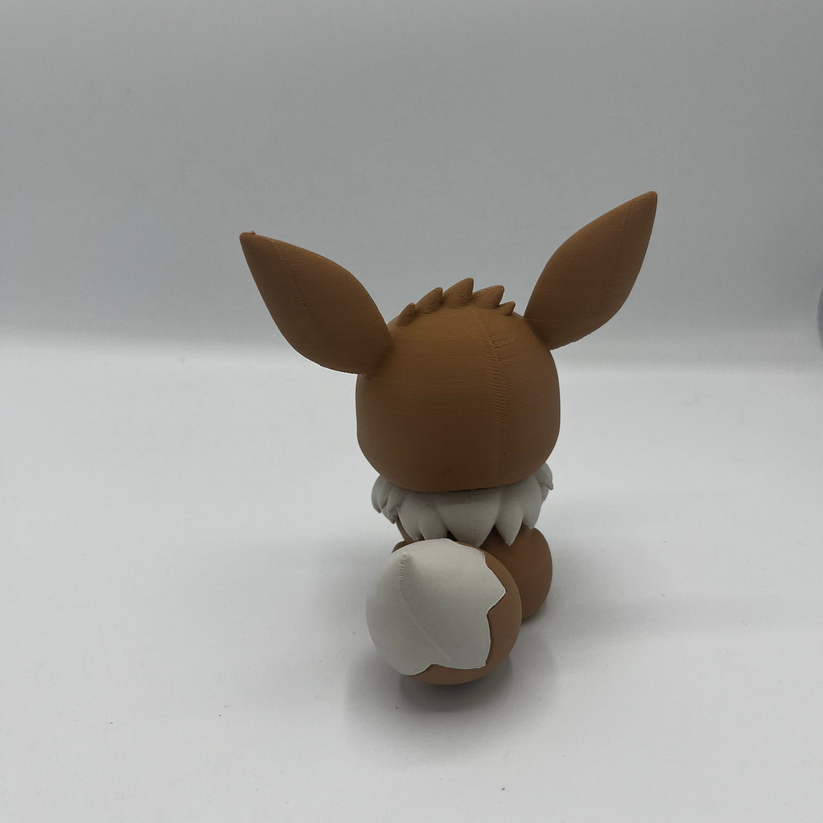 A small brown and white figurine of an animal character with long ears, shown from the back on a plain light studio background.