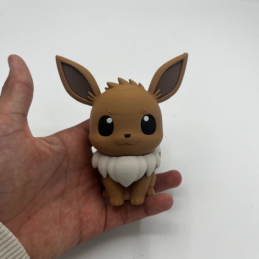 A small brown and white Eevee figurine being held in a person's hand against a plain light background.