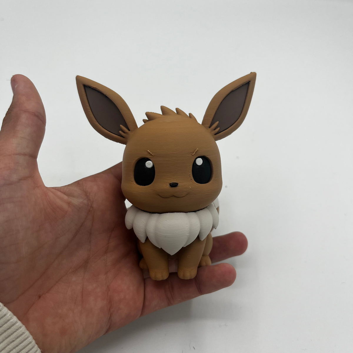 A small brown and white Eevee figurine being held in a person's hand against a plain light background.