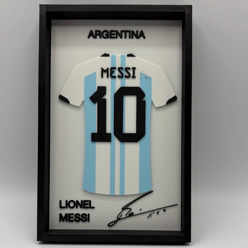 A framed Lionel Messi Argentina number 10 jersey display on a light gray background. The black shadowbox frame contains a white and light blue striped Argentina jersey with 'MESSI' and '10' in black, plus 'ARGENTINA' at the top and 'LIONEL MESSI' with a signature at the bottom.