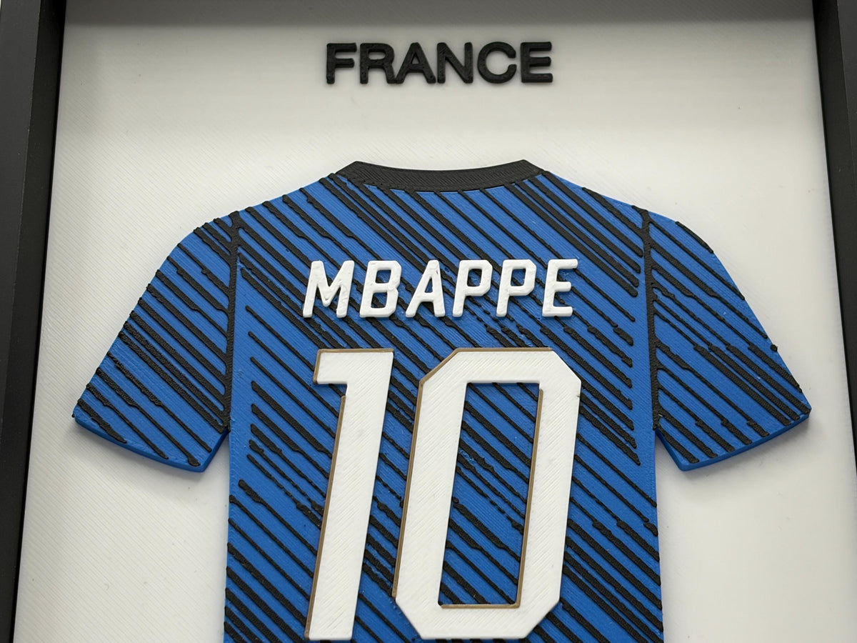 A framed display featuring a blue and black striped France national team jersey with 'MBAPPE' and the number '10' on the back, mounted under a black-framed glass panel with 'FRANCE' at the top.