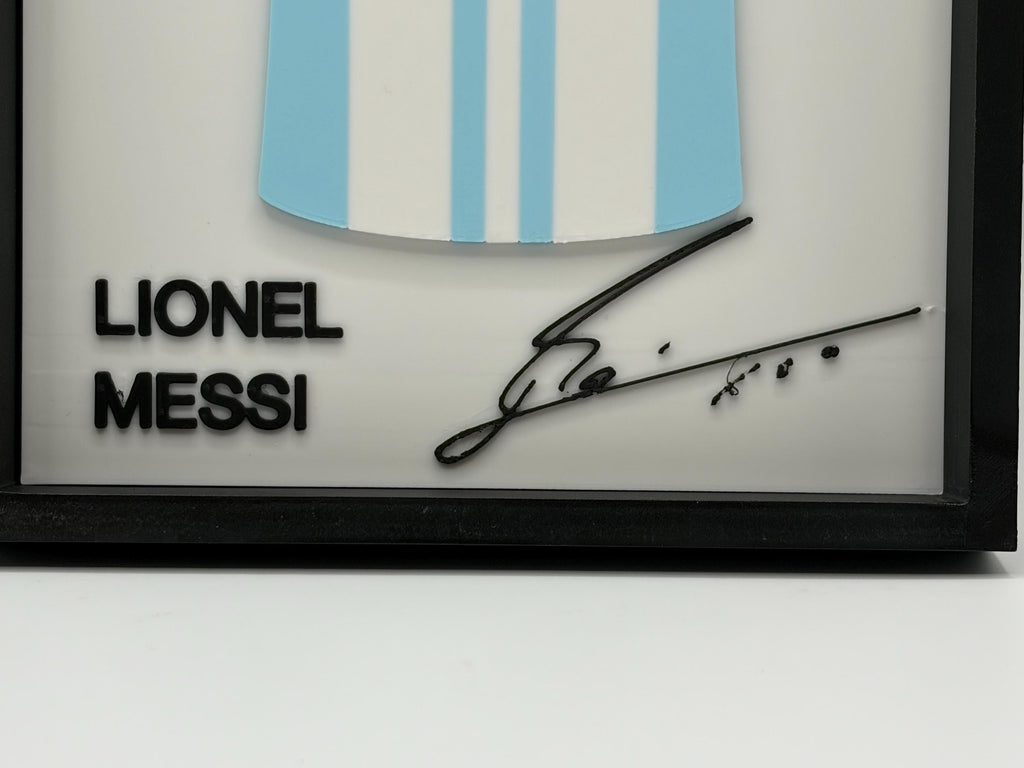 A framed Lionel Messi collectible plaque featuring a light blue and white striped Argentina soccer jersey graphic, his name in bold black letters, and a black autographed signature on a white background inside a black frame.