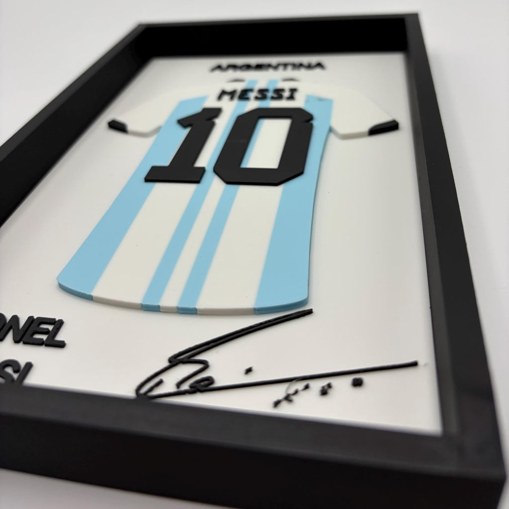 A framed Argentina number 10 Messi wall decor piece, featuring a light blue and white striped soccer jersey with black lettering and signature, displayed in a black frame.