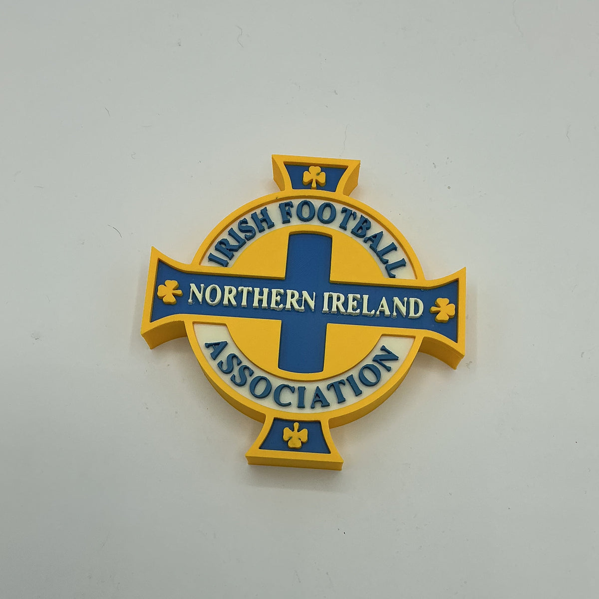 A Northern Ireland Irish Football Association badge featuring a yellow and blue Celtic cross design with the text 'NORTHERN IRELAND ASSOCIATION' and 'IRISH FOOTBALL' on a light gray background.