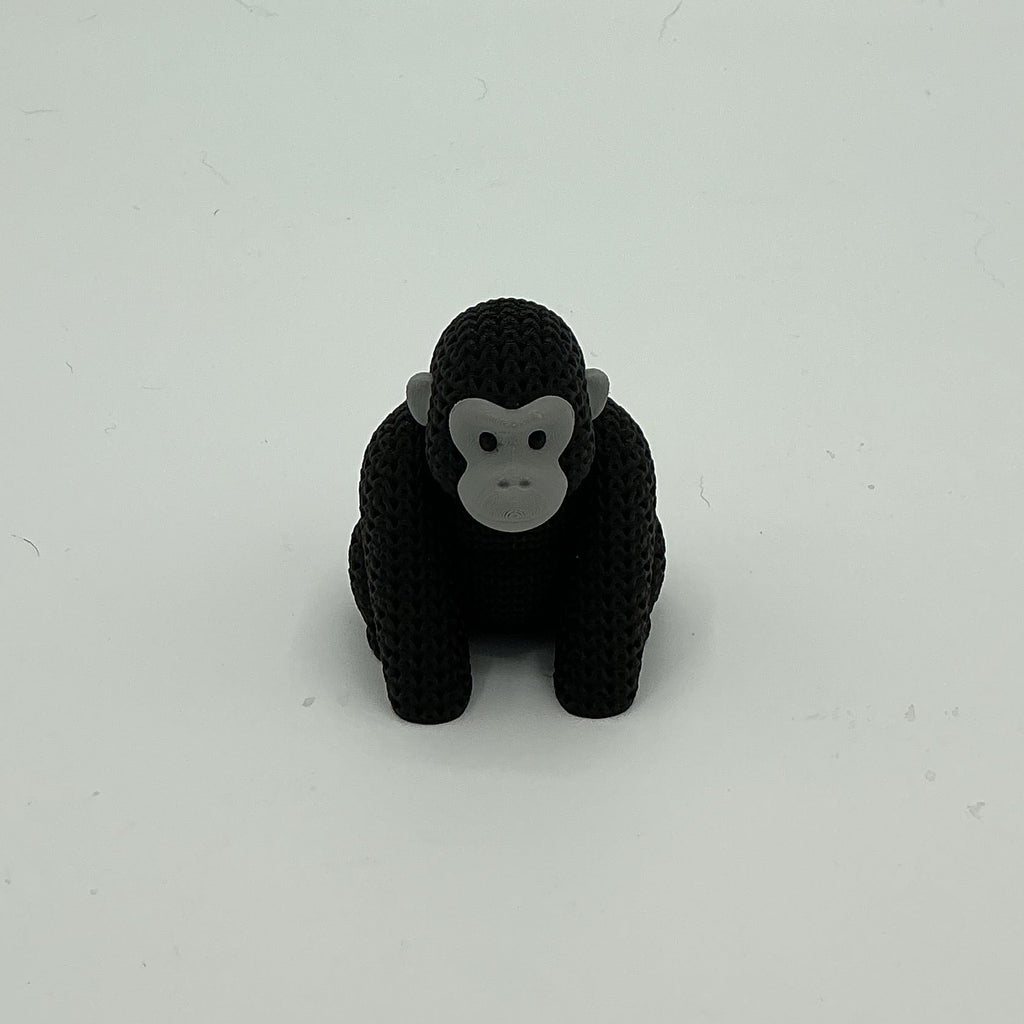 A small black knitted-style gorilla figurine with a gray face, standing upright on a plain light grey background.