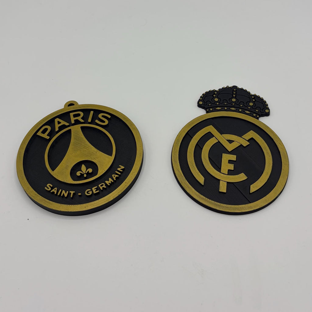 Two round Paris Saint-Germain and Real Madrid soccer badges shown side by side on a plain white background.