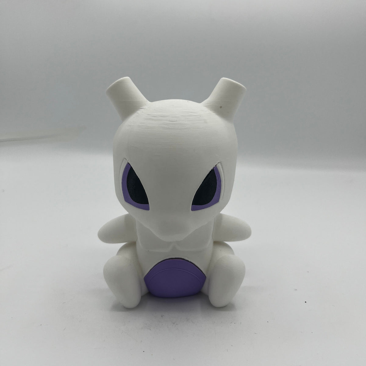 A small white character figurine with large black eyes outlined in purple and a purple belly, centered on a plain light studio background.