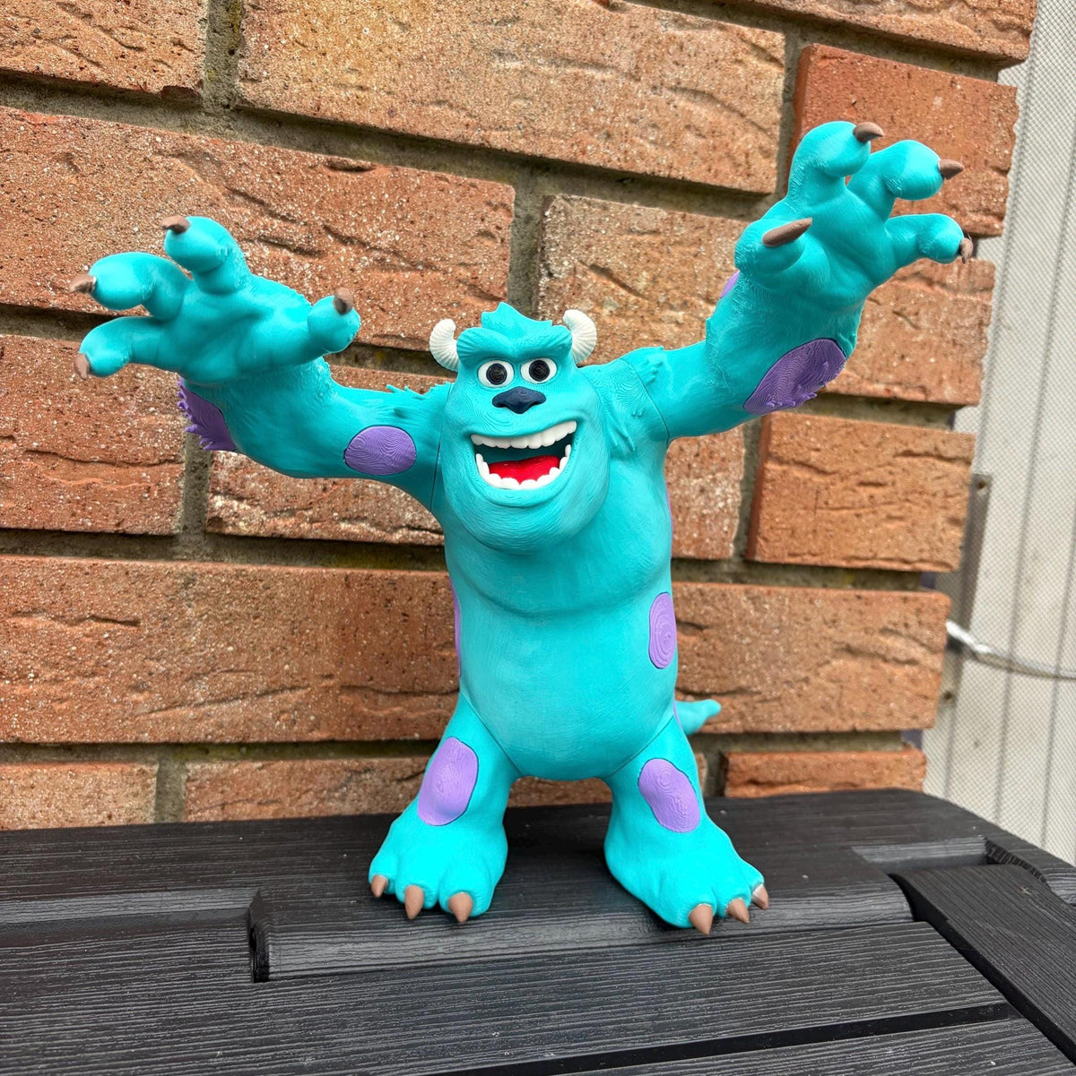 A colourful toy figurine of a blue monster with purple patches and white horns, standing on a dark wooden surface in front of a brick wall.