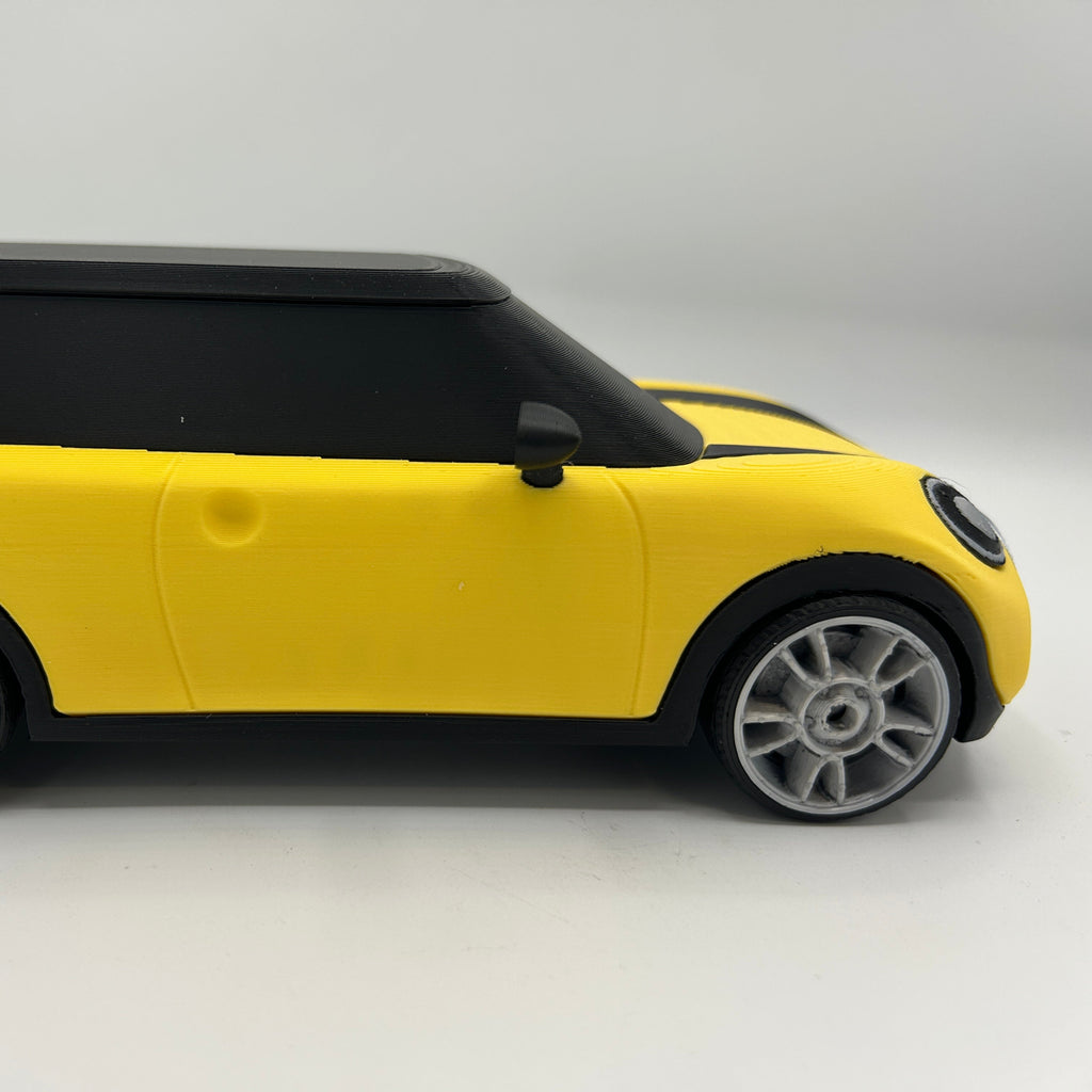 A yellow and black toy car with silver multi-spoke wheels, shown from a side profile view against a plain light grey background.