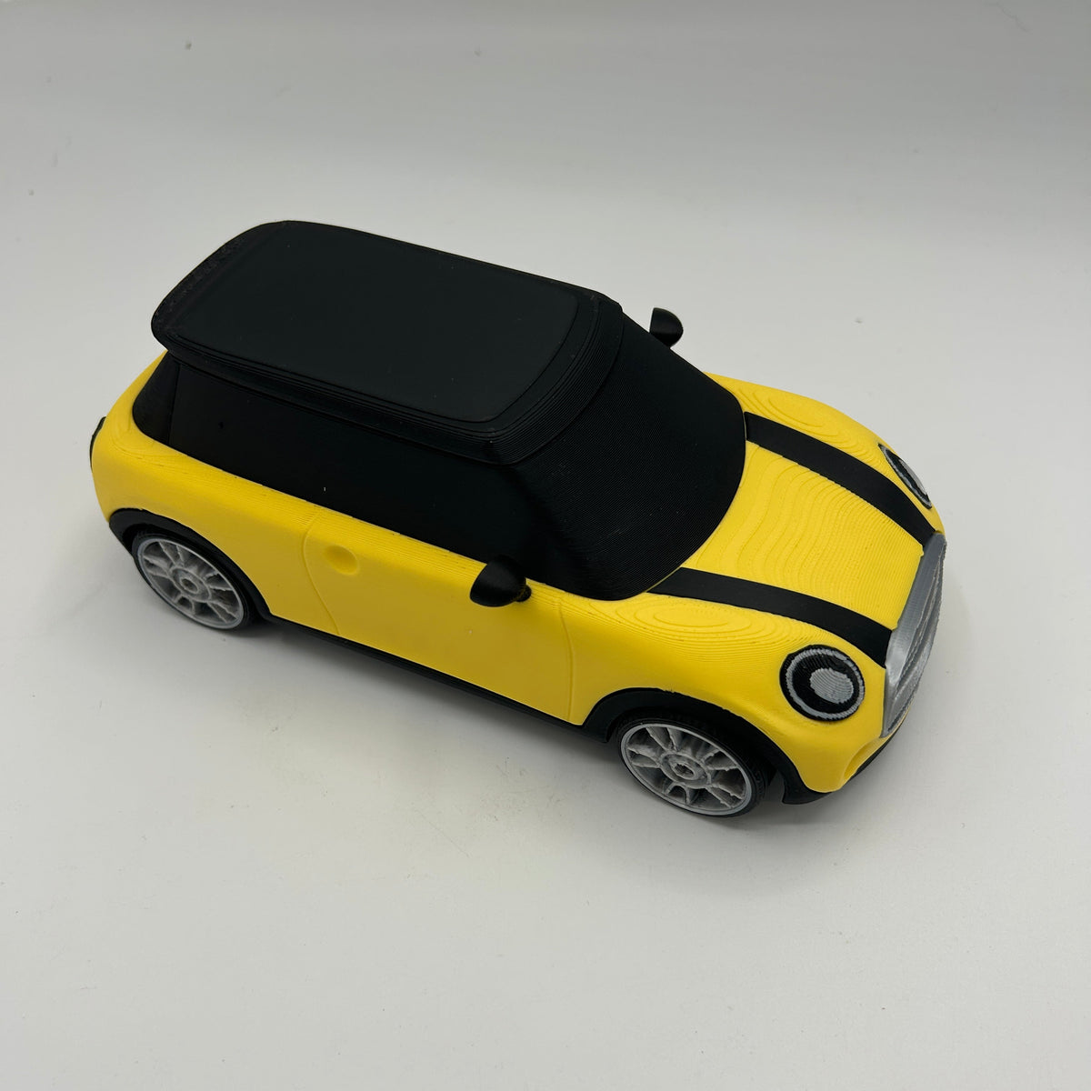 A yellow and black toy car with a black roof, styled like a classic Mini Cooper, photographed on a plain light grey background.