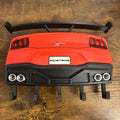 A red and black Mustang rear spoiler wing accessory with a white Mustang badge, displayed on a wooden table.