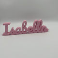 A pink 3D printed name sign spelling 'Isabella' in a cursive font, shown on a neutral gray background.
