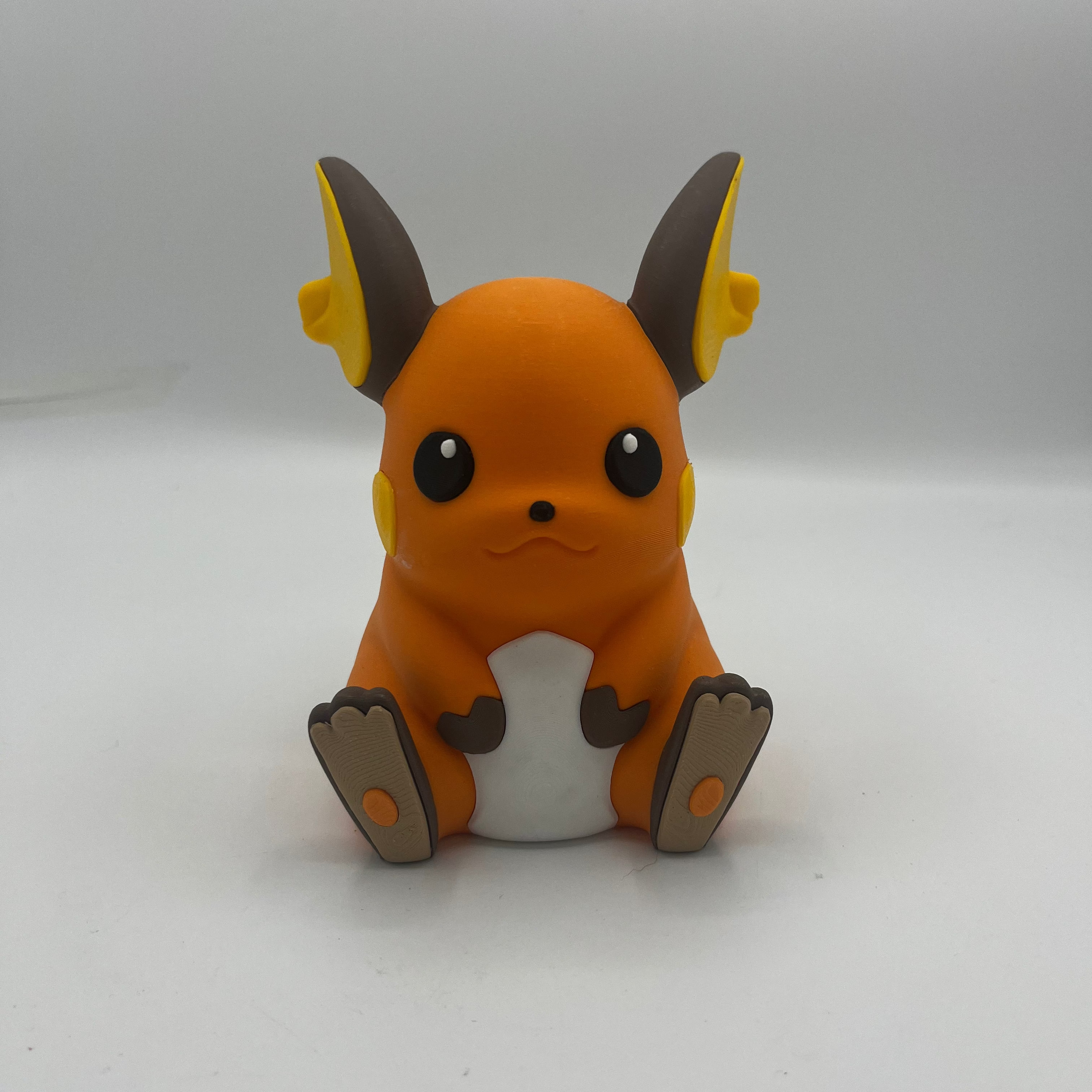 A small orange and white cartoon character figurine with brown and yellow pointed ears, sitting upright on a plain light background.