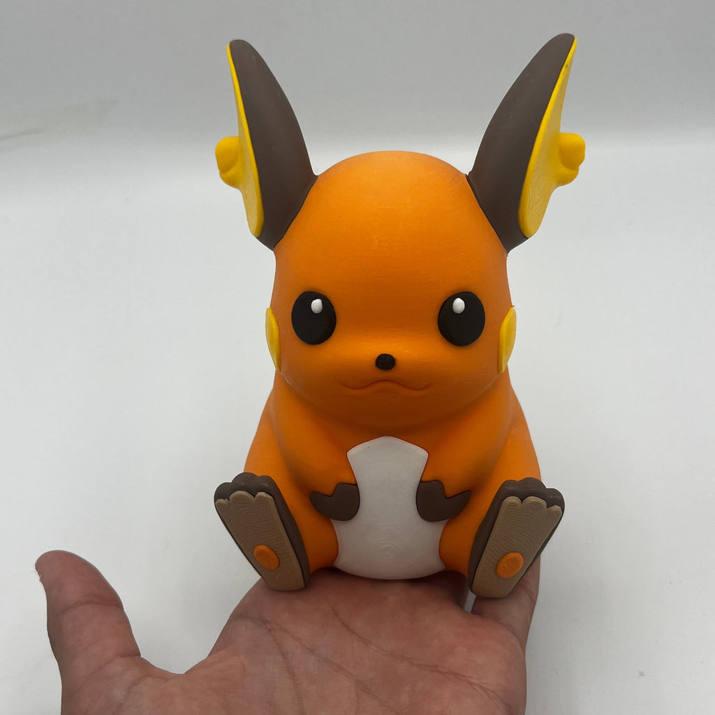 An orange and white Raichu figurine with brown and yellow accents, sitting on a person's hand to show its size against a plain white background.