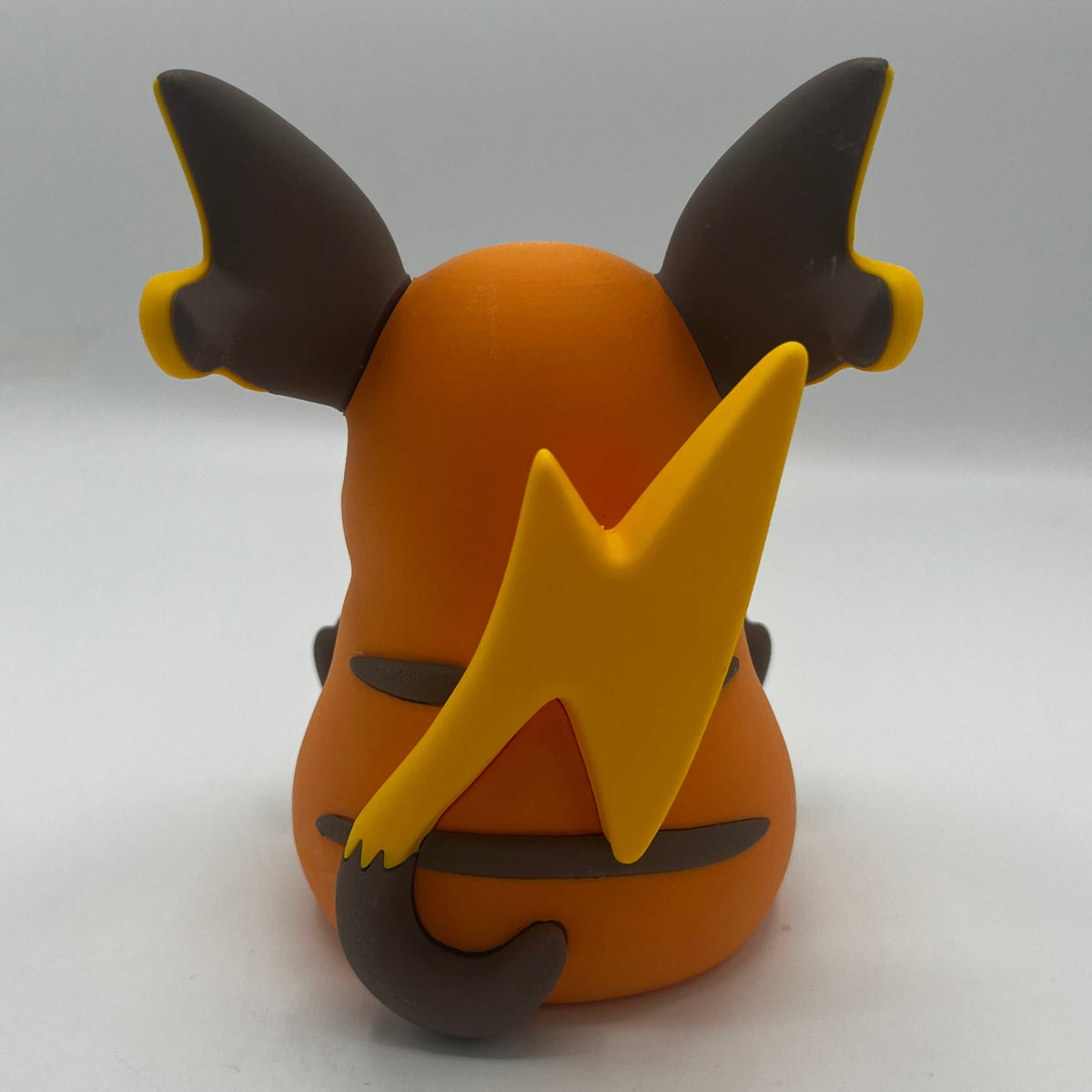 An orange and yellow clay figure of a Pokémon character, shown from the back against a plain light gray background.