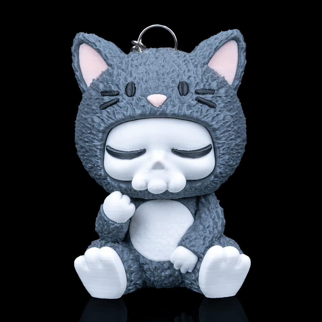 Gray cat-shaped keychain with a skull face on a black background