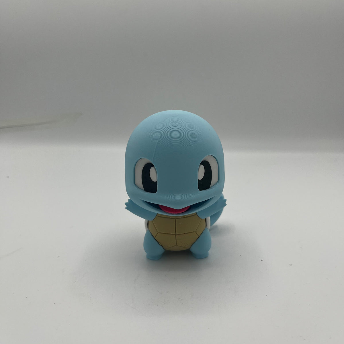 A small blue Squirtle toy figure with a tan shell and black eyes, standing against a plain light background.