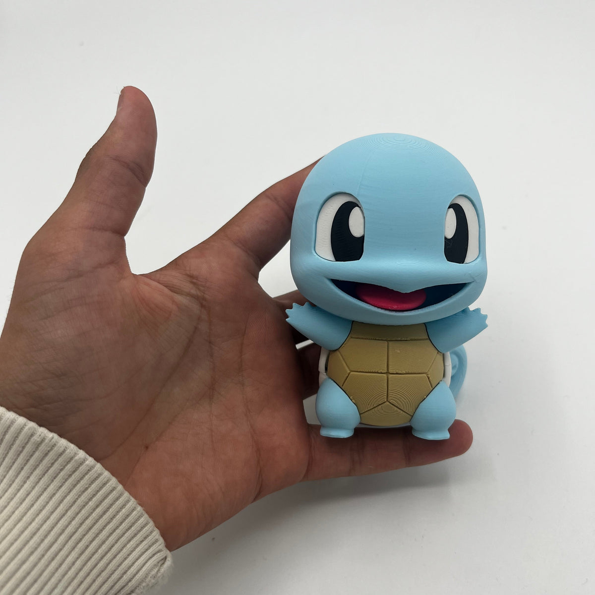 A small blue Squirtle figurine held in a person's hand against a plain white background.