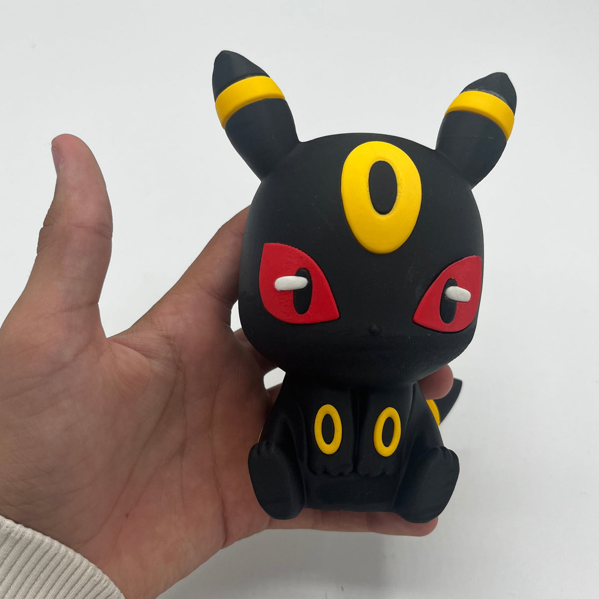 A black Umbreon figurine with yellow and red details, held in a person's hand against a plain white background.