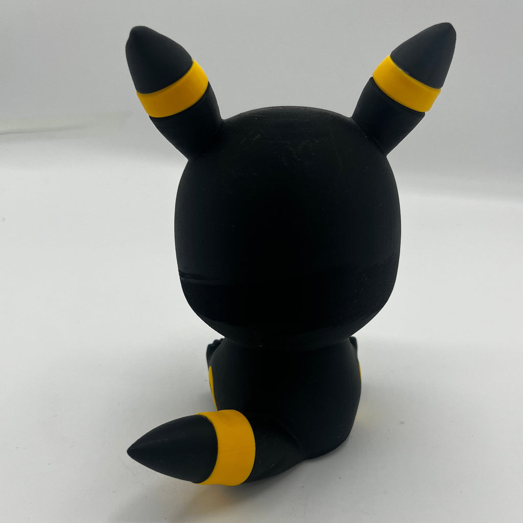 A black vinyl figure of a Pokémon character, shown from the back, featuring yellow and black striped accents on its ears and tail, set against a plain white background.