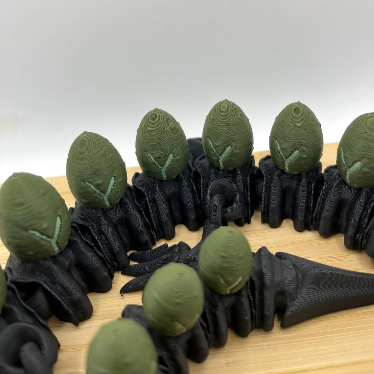 A close-up of a black 3D-printed ring featuring green leaf-shaped accents arranged in a circle on a light wood surface against a white background.