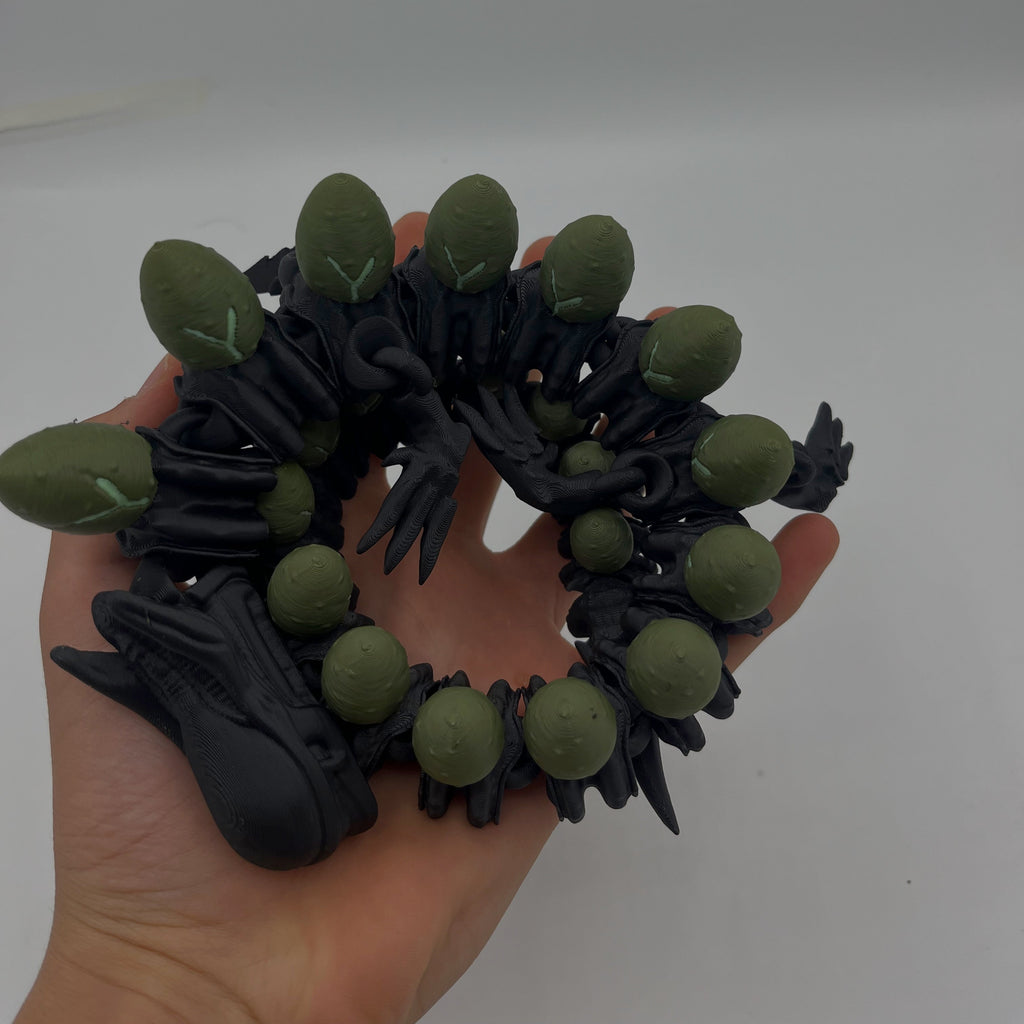 A black and olive green multi-headed serpent or dragon figurine being held in a person's hand against a plain light grey background.