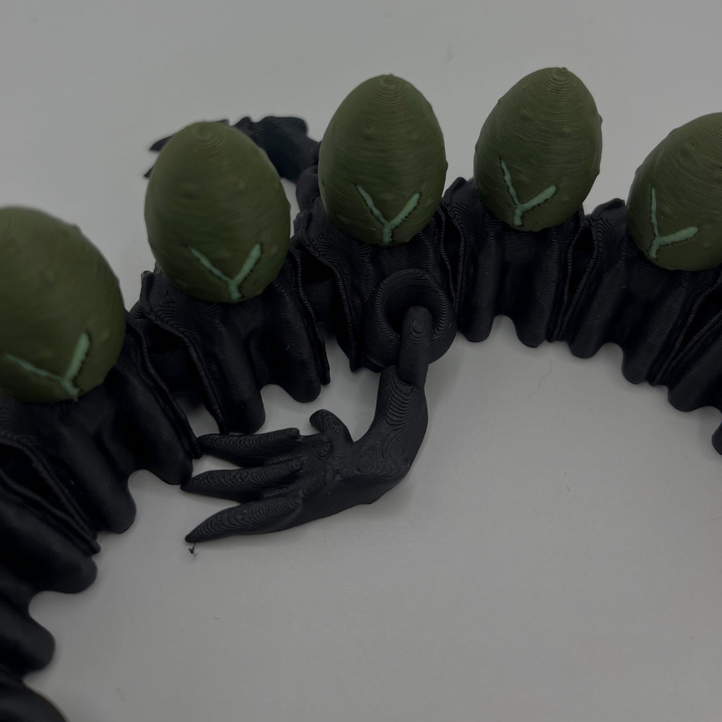 A close-up of a black rubber or silicone accessory featuring five green oval shapes arranged along the top, with a small black claw-like detail in the center, photographed on a plain light background.