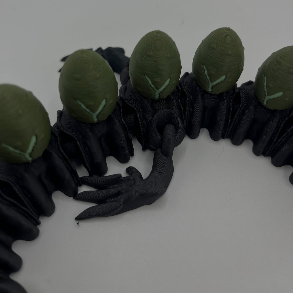 A close-up of a black rubber or silicone accessory featuring five green oval shapes arranged along the top, with a small black claw-like detail in the center, photographed on a plain light background.