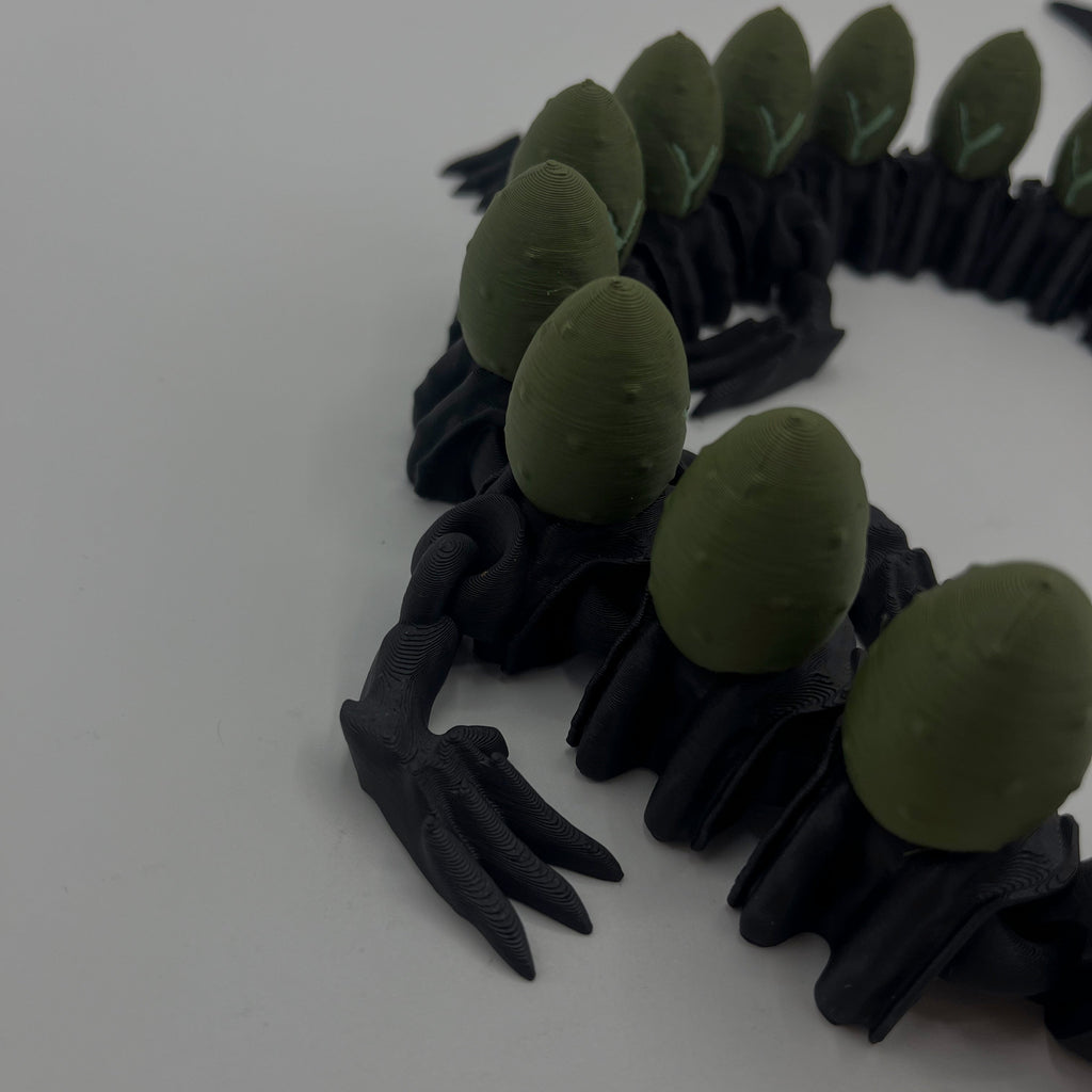 A black clawed creature or monster accessory with multiple olive green egg-shaped back plates, photographed on a plain light background.