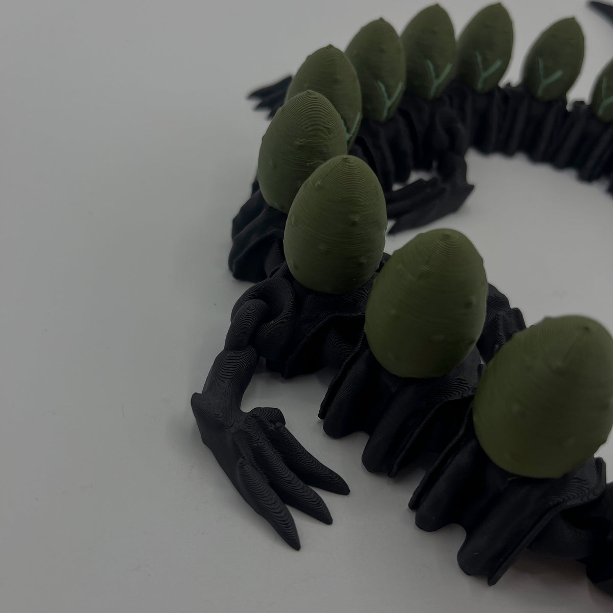 A black clawed creature or monster accessory with multiple olive green egg-shaped back plates, photographed on a plain light background.