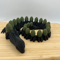A black dragon figurine with green scales, displayed on a light wood cutting board against a plain white background.